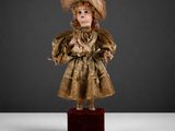 une poupée ancienne représentant une femme vêtue d'une robe dorée et d'un chapeau