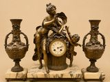 une statue représentant une femme assise sur une table, à côté de trois vases et d'une horloge