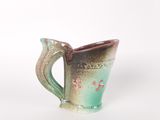 une tasse verte et marron avec une anse, posée sur un fond blanc