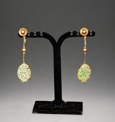 une paire de boucles d'oreilles en jade et en or posée sur un socle noir