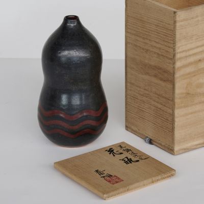 un vase noir et une boîte en bois posés sur une surface blanche