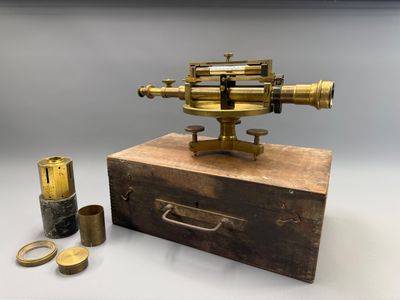 un microscope ancien en laiton posé sur une boîte en bois, avec une paire de rubans adhésifs