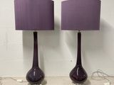 une paire de lampes de table en verre violet, avec des abat-jours violets, posées sur une étagère