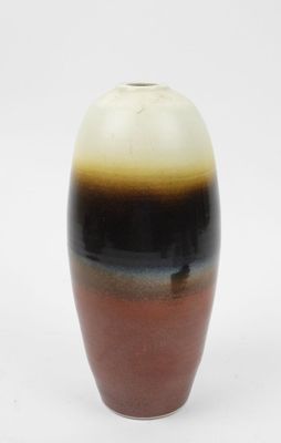 un vase brun et noir posé sur une surface blanche