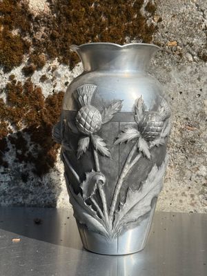 un vase en argent posé sur une table, avec un mur en pierre en arrière-plan