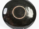 a black plate with a brown rim on a white surface