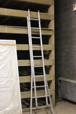 une échelle appuyée contre un mur, à côté d'une pile de palettes