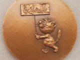 une médaille d'or sur laquelle figure un chat tenant une pancarte