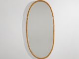 un grand miroir ovale avec un cadre en bambou accroché au mur