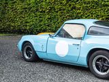 a blue and yellow sports car parked in front of a hedge