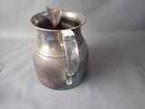 a silver pitcher with a spoon in it sitting on a table