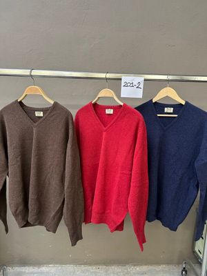 trois pulls suspendus à un portant dans un magasin de vêtements