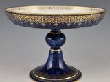 un plat à gâteau ancien bleu et or, muni d'un pied et posé sur un socle