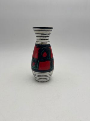 petit vase rouge et noir posé sur une table blanche, sur fond gris