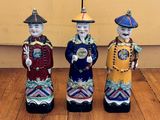 trois figurines en céramique représentant des hommes asiatiques debout sur un plancher en bois