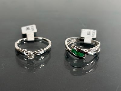 two silver rings with emerald stones on them sitting on a table