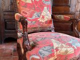 a red chair with a colorful upholstered seat in front of a wooden cabinet