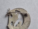 a silver brooch with a cat and a bird on it