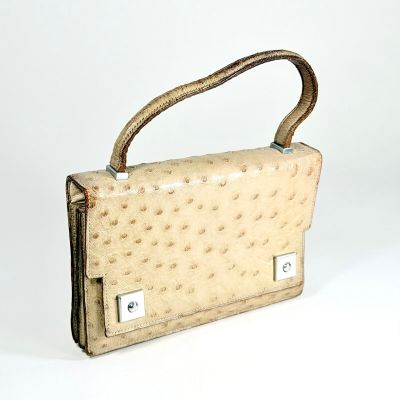 sac à main en cuir d'autruche beige avec des anses en métal sur un fond blanc