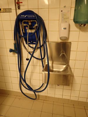 un tuyau bleu fixé au mur de des toilettes publiques