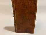 an old brown book sitting on top of a table next to a white wall