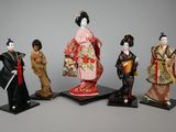 four figurines of geisha dolls are standing on a stand