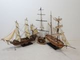 two wooden model ships with sails are sitting on a white surface