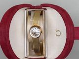 une montre dans un coffret rouge, avec un bracelet doré