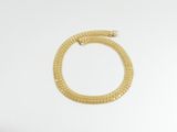 un bracelet en or posé sur une surface blanche, sur fond blanc