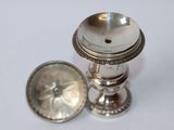 a small silver object on a white surface next to a coin