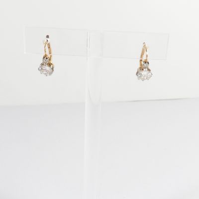 une paire de boucles d'oreilles en or et diamants, présentée sur un présentoir transparent