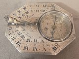 a silver clock with roman numerals on it on a table