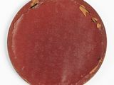 an old red plate sitting on top of a white surface