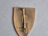 a close up of a gold pin with a knife on it