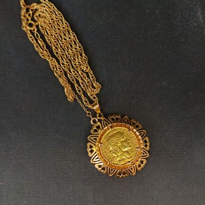 Gros plan sur un collier en or sur lequel se trouve une pièce de monnaie