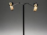 a pair of gold and black earrings on a black stand
