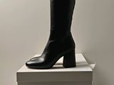 une paire de bottes en cuir noir posée sur une pile de cartons blancs
