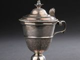une coupe ancienne en argent avec un couvercle, posée sur une surface noire