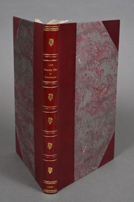 an old book with a red cover and gold trim sitting on a gray surface