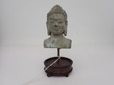 statue représentant une tête de Bouddha posée sur un socle en bois, sur une surface blanche