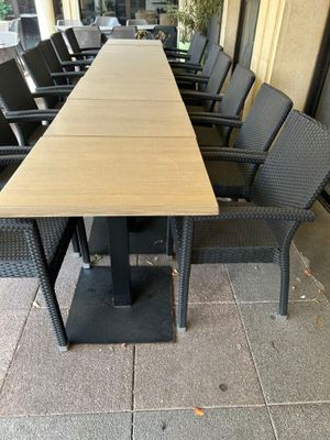 une longue table entourée de nombreuses chaises, sur le trottoir