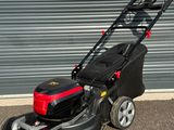 une tondeuse à gazon noire et rouge garée devant la porte d'un garage