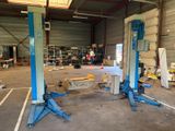 two blue lifts in a garage with a man standing in the background