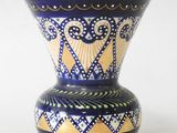 un vase bleu et or posé sur une surface blanche
