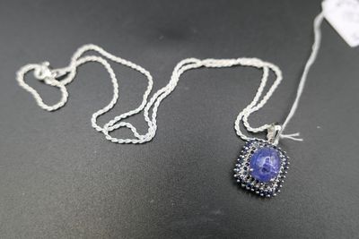 une chaîne en argent avec un pendentif orné d'une pierre bleue, posée sur une surface noire