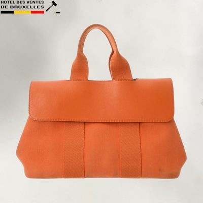 an orange leather handbag with a long strap on a white background