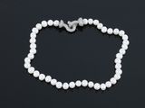 un collier de perles blanches muni d'un fermoir en argent, posé sur un fond noir