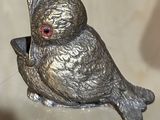 figurine en argent représentant un oiseau aux yeux rouges, posé sur une table en verre