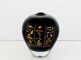 a black vase with gold writing on it on a white surface