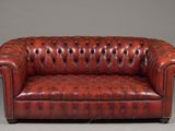 a red leather chesterfield sofa sitting on top of a gray floor